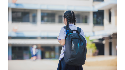 A young girl walks towards a school building with a blue pack on her back