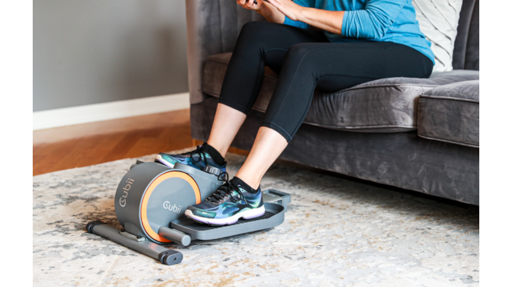 A woman uses the Cubii Go while seated on her couch
