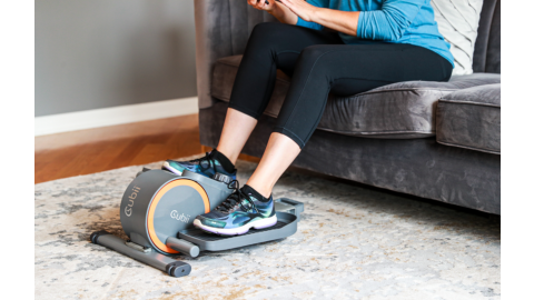A woman uses the Cubii Go while seated on her couch