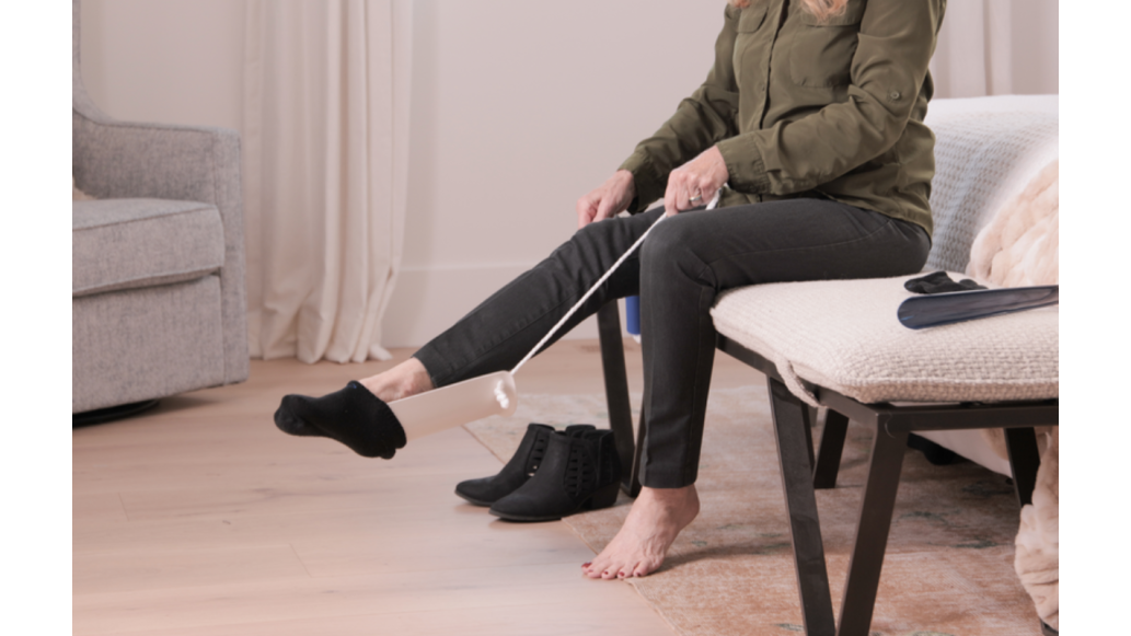 A woman uses a sock aid to pull on her black sock