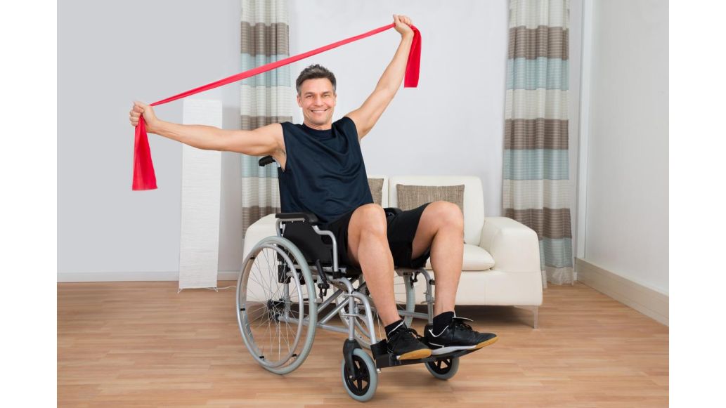 Man in wheelchair holding a red resistance band in his hands with his arms stretched wide