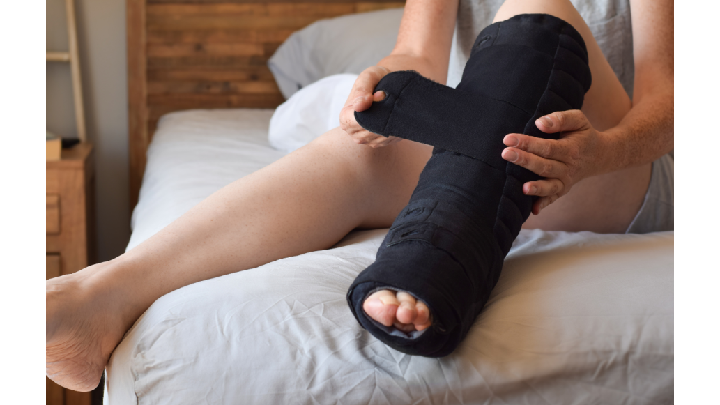A woman sitting on a bed  applies a black lymphedema wrap to her leg.