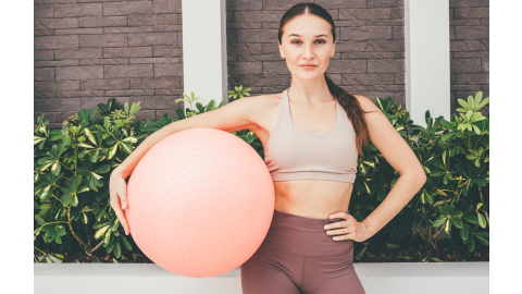 A woman stands outside holding a pink exercise ball