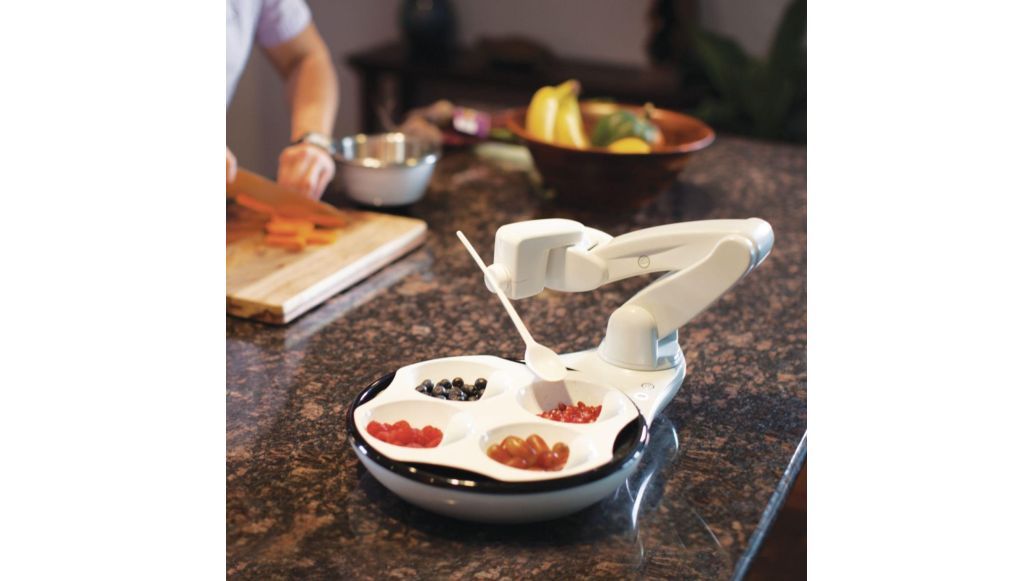 Obi Robotic feeder on kitchen counter, holding spoon ready to pick up various fruits.
