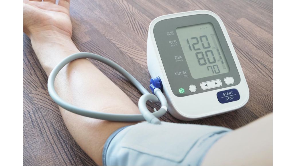 Close up of an arm in a blood pressure cuff that's attached to a portable blood pressure monitor with digital display screen.