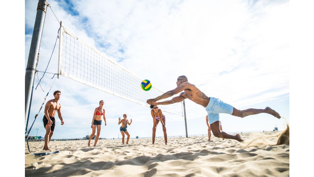 Group of people playing beach volleyball on sunny day.