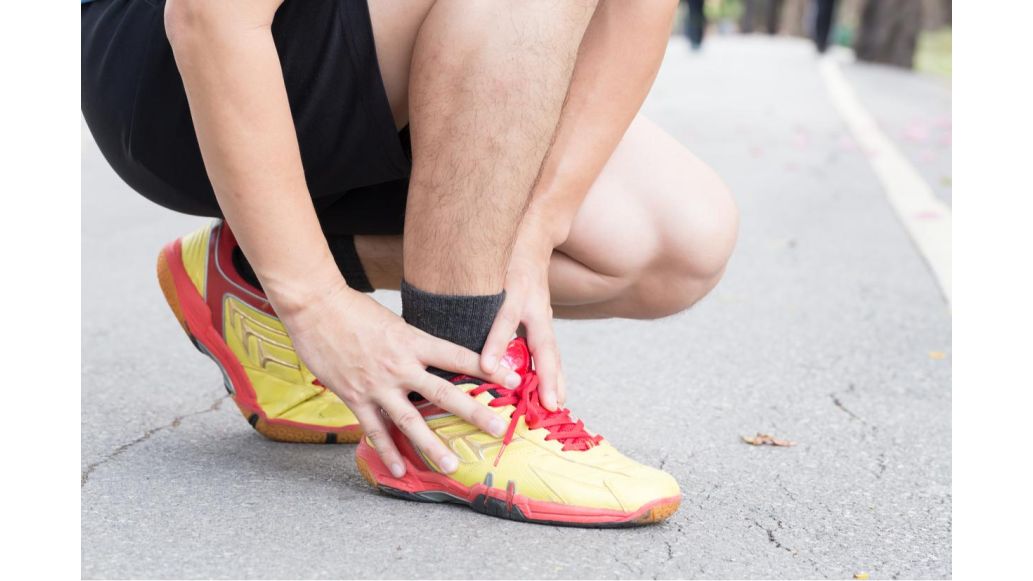 Person reaching down, grabbing onto ankle and athletic sneaker as if in pain.