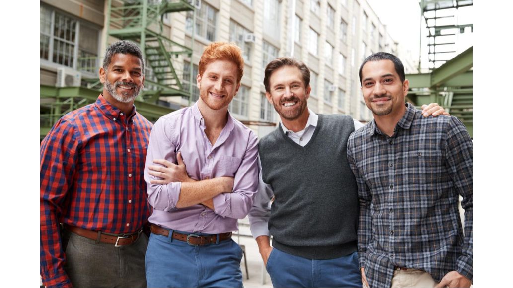 4 men standing outside of a city building, smiling.