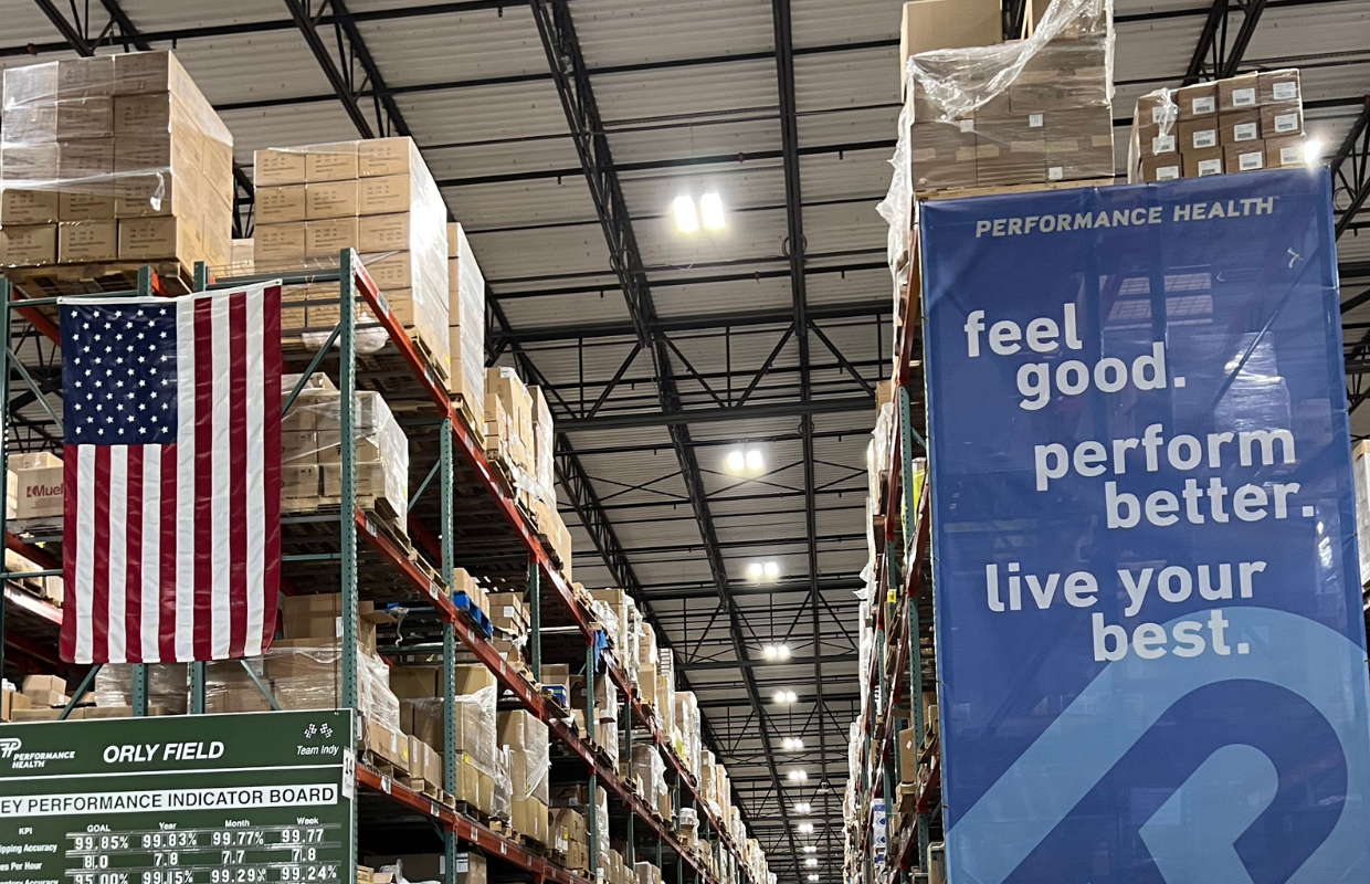 An image of a Performance Health warehouse with an American flag hanging and a banner reading "Feel Good, Perform Better, and Live Your Best" 