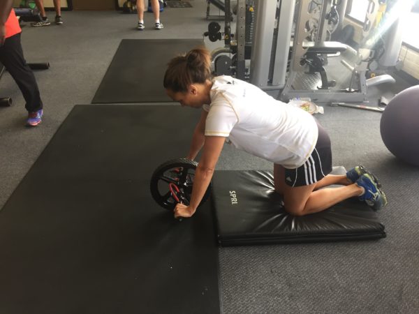 person in starting position for reverse hyperextension exercise, holding exercise wheel with knees on an exercise mat