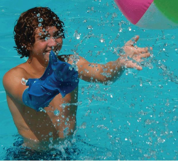Boy with right arm cast makes a splash in the pool while throwing a beach ball thanks to his Dry Pro waterproof cast cover
