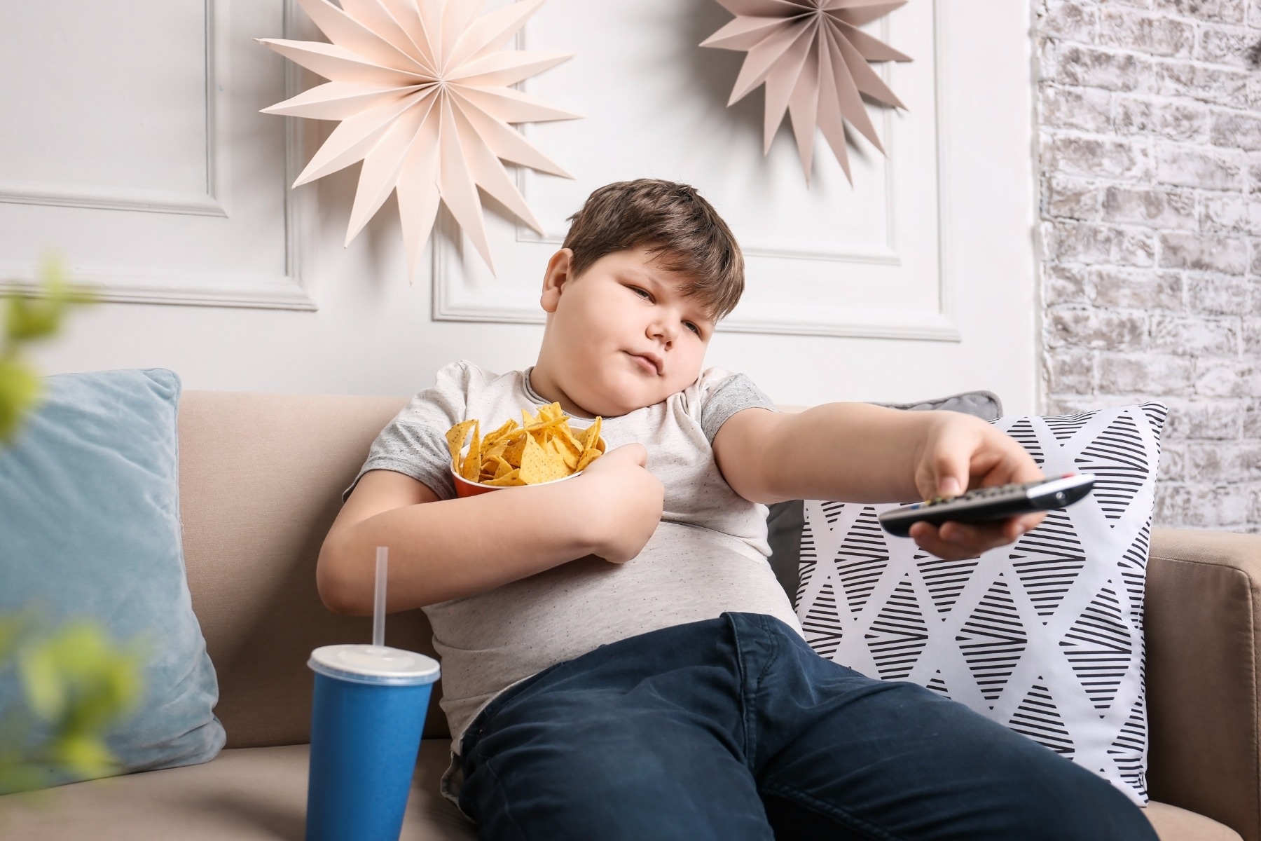 overweight boy watching tv and eating snacks