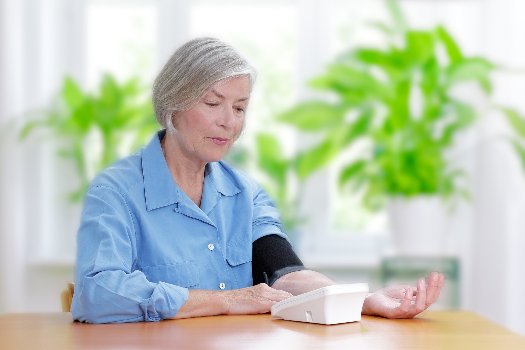 Senior woman sitting at table using a blood pressure monitor