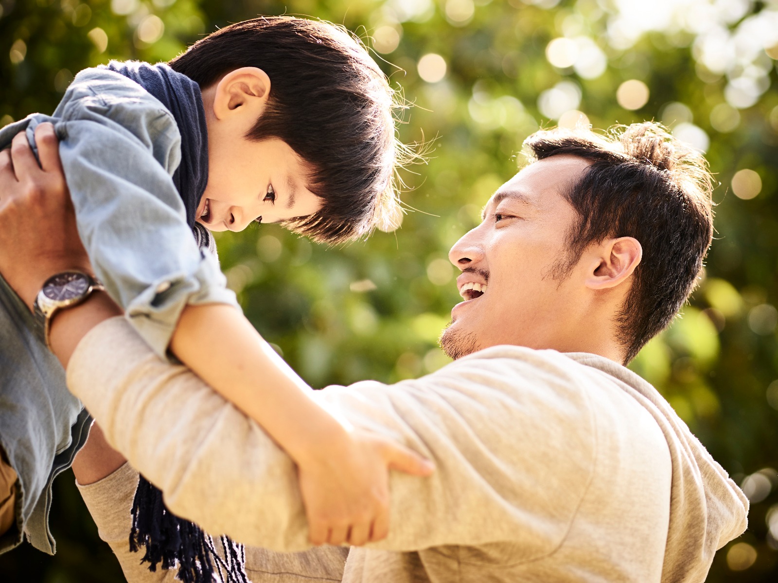 Father holding up his young son outside, both of them smiling and having fun