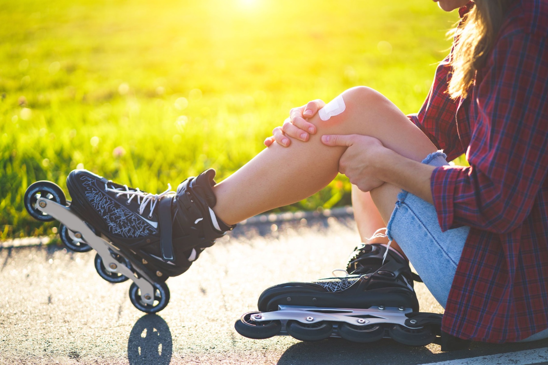 Woman seated on ground, wearing roller blades and holding knee with bandage on knee cap