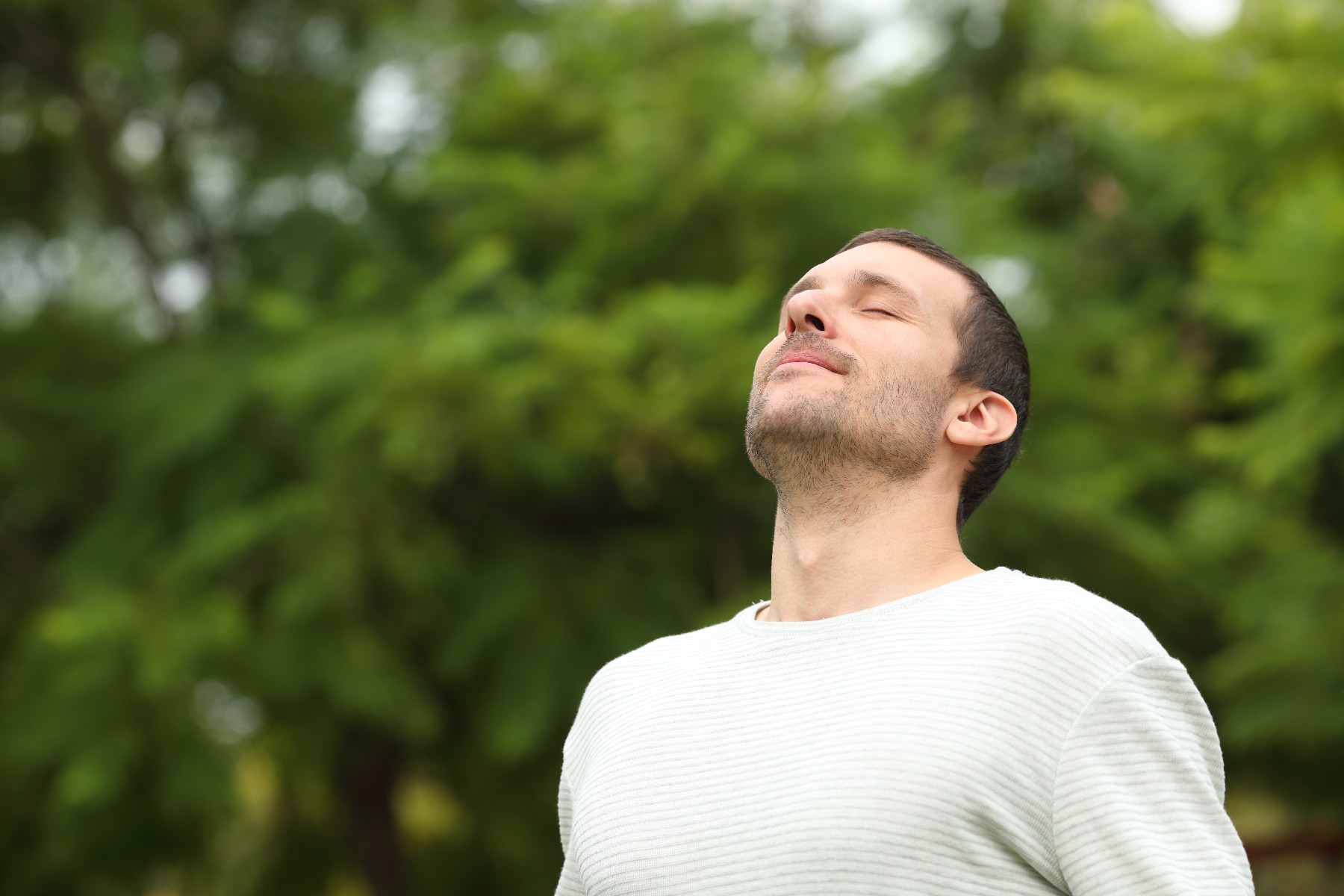 Man standing outside, looking up towards the sky peacefully with a smile on his face