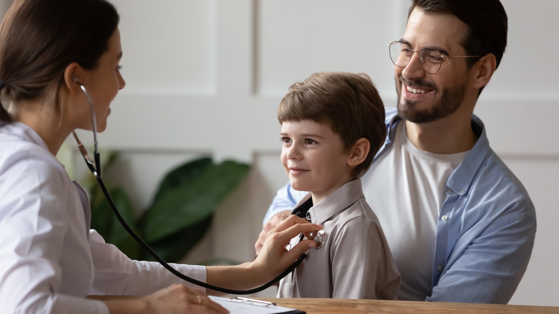 Young boy held by his dad as a Doctor examines him with her stethoscope