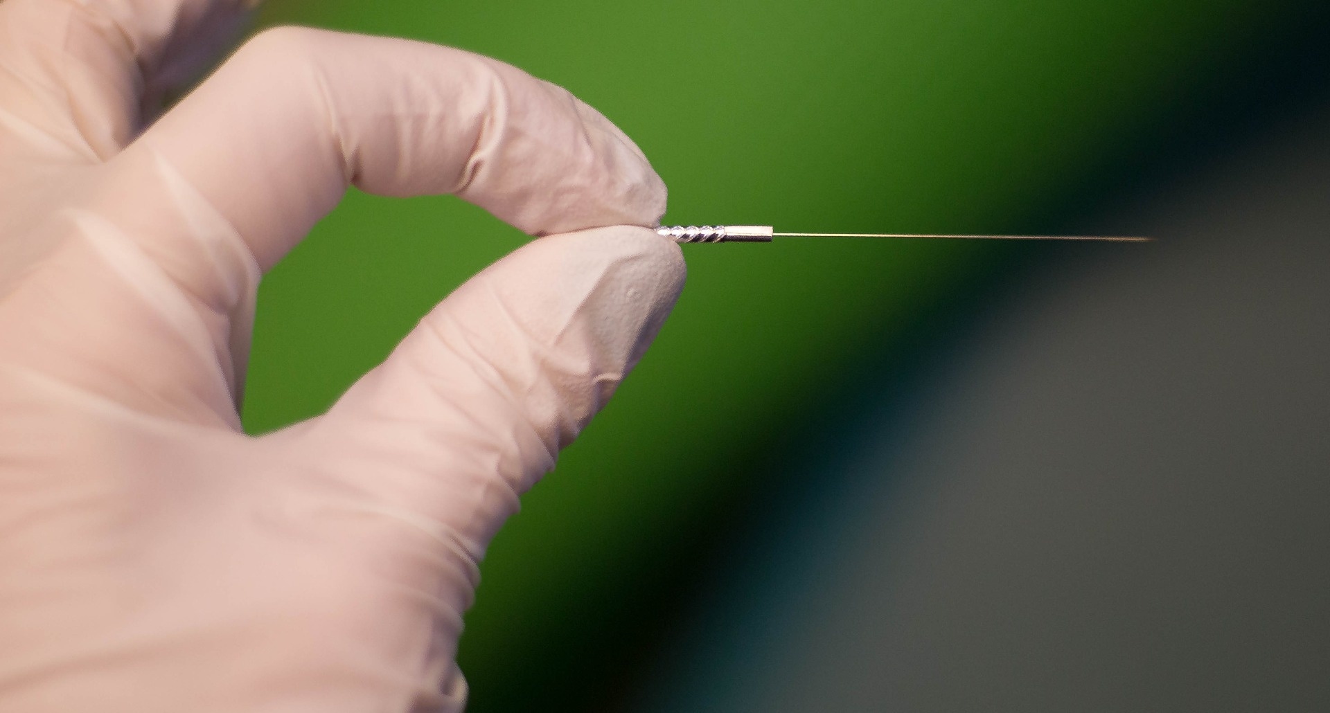 Person wearing a glove holding a dry needling needle, seen up close