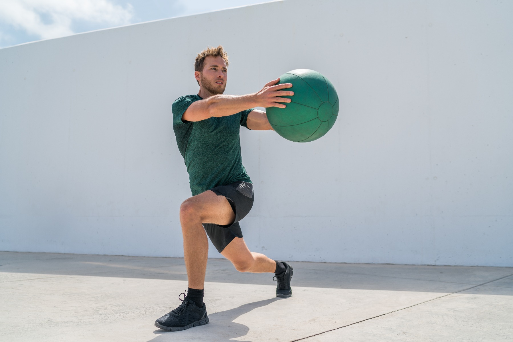 Man holding exercise ball doing twisted lunge exercise